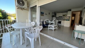 Un balcó amb una taula i cadires, una porta corredissa de vidre que dona a una cuina i un aparell d'aire condicionat.
