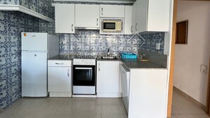 Cuina pràctica amb armaris blancs, microones, fogó i rentaplats. Les parets tenen un disseny de rajola amb motius blaus i blancs.