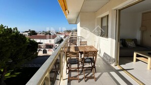 Un balcón con una mesa y sillas de madera, vistas a la ciudad y una puerta que da paso a un espacio interior con un sofá y una lámpara.