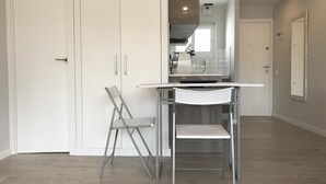 A modern kitchen with white cabinetry, a stainless steel sink, and a dining area with a white table and metal chairs. - Estudio Reformado Regueral - 123A (Cambrils)