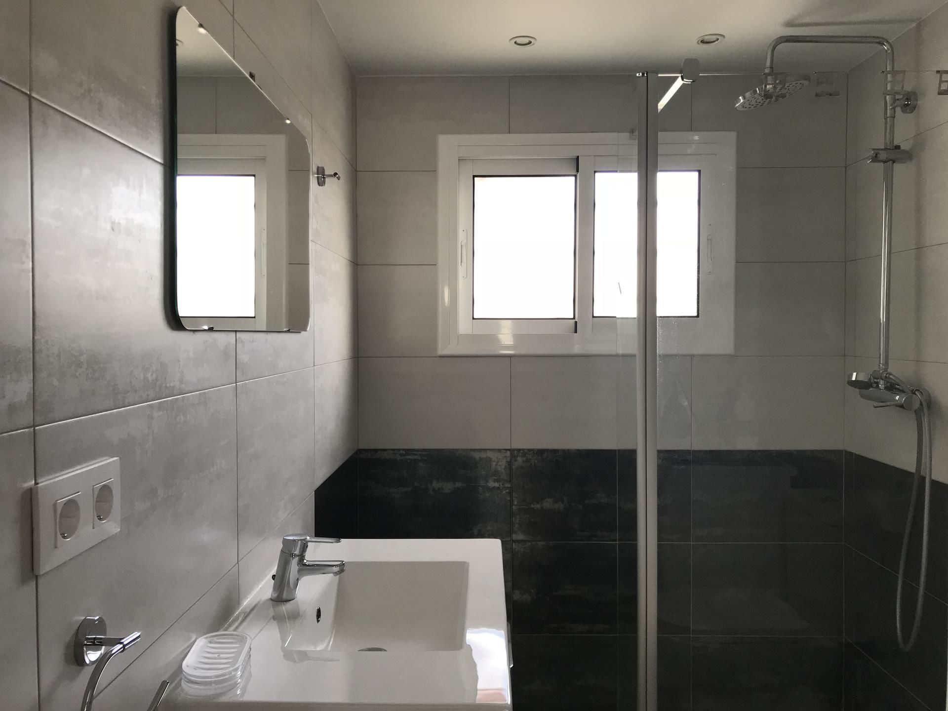 Un baño moderno con un espejo grande, un lavabo y una ducha.