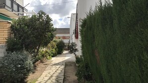 A narrow stone pathway flanked by lush greenery and buildings with balconies. - Estudio Reformado Regueral - 123A (Cambrils)