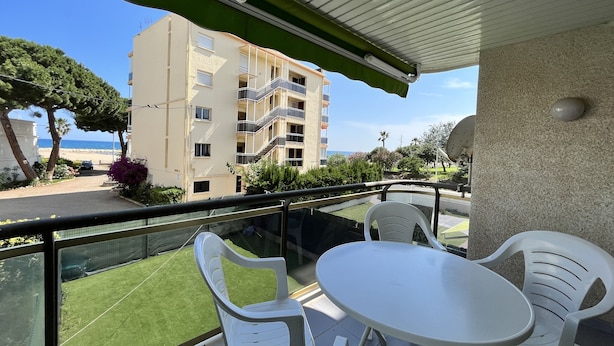 A balcony with a table and chairs, overlooking a beach and a building. - Apartamento Cambrils Park - 104B (Cambrils)