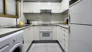 A compact kitchen with white cabinets, a built-in oven, a washing machine, and a microwave. - Apartamento Cambrils Park - 104B (Cambrils)