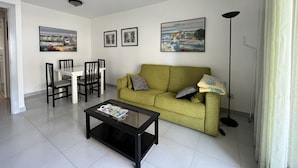 A living room with a green sofa, a coffee table, a dining table with chairs, and framed pictures on the wall. - Apartamento Cambrils Park - 104B (Cambrils)