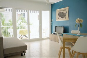 A bright room with a blue wall, a map of the USA, a dining table with chairs, and a sofa. - Apartamento Horta Sta María - 107B (Cambrils)