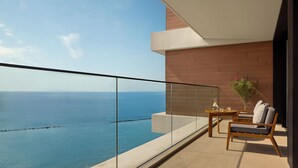 A balcony with a view of the sea, a table with chairs, and a potted plant.