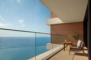 A balcony with a view of the sea, a table with chairs, and a potted plant.