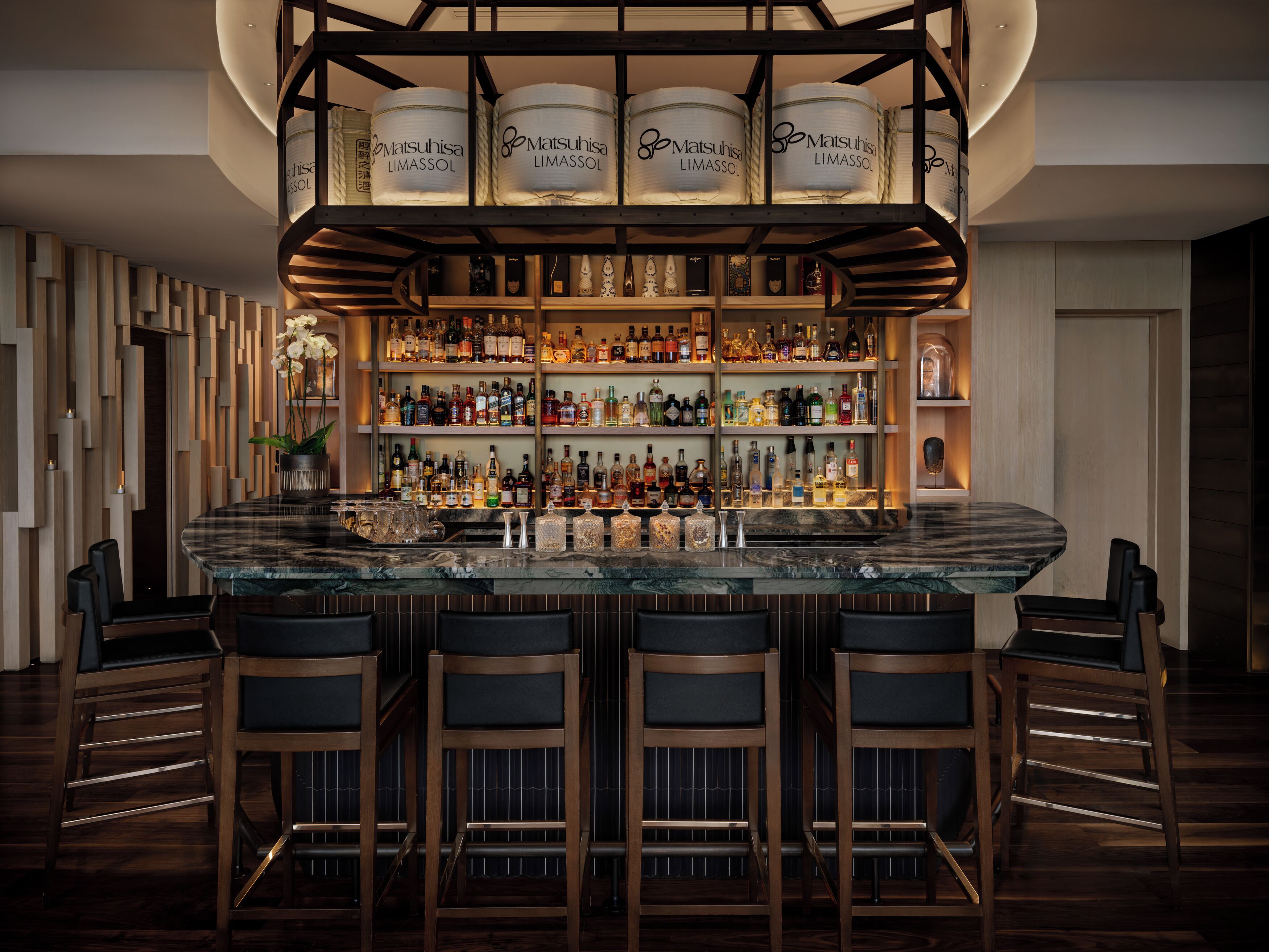 A bar area with a marble countertop, multiple liquor bottles, and bar stools.