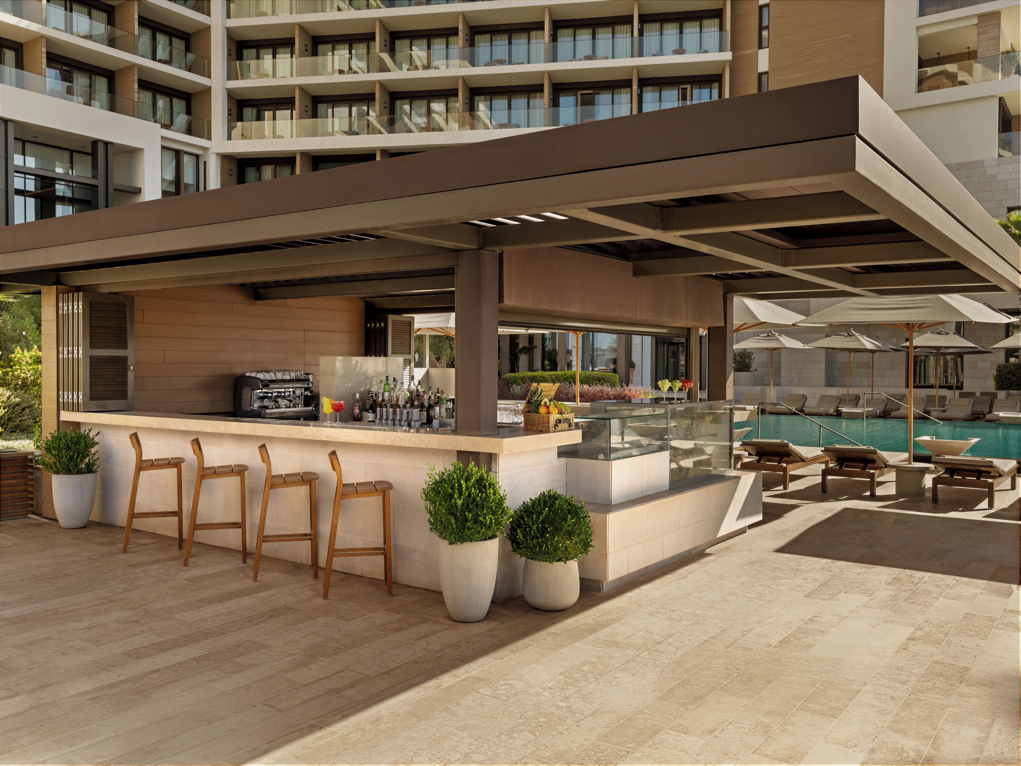 A modern outdoor bar area with seating, a pool, and a view of the building's interior.
