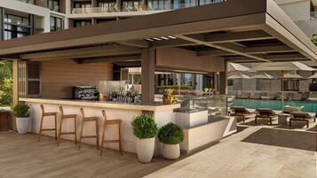 A modern outdoor bar area with seating, a pool, and a view of the building's interior.