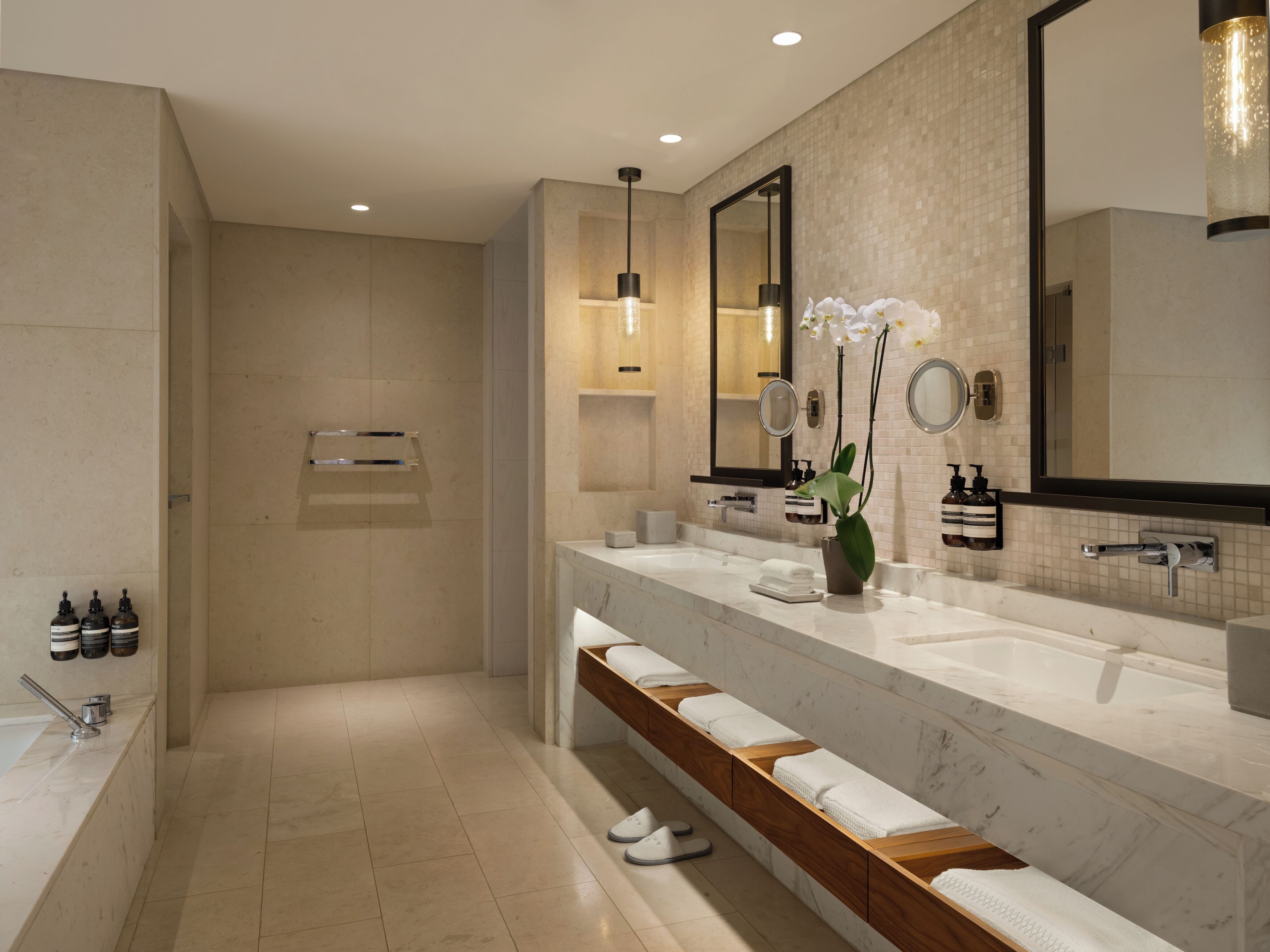 Un baño moderno con un espejo grande, un tocador con encimera de mármol y una zona de ducha.