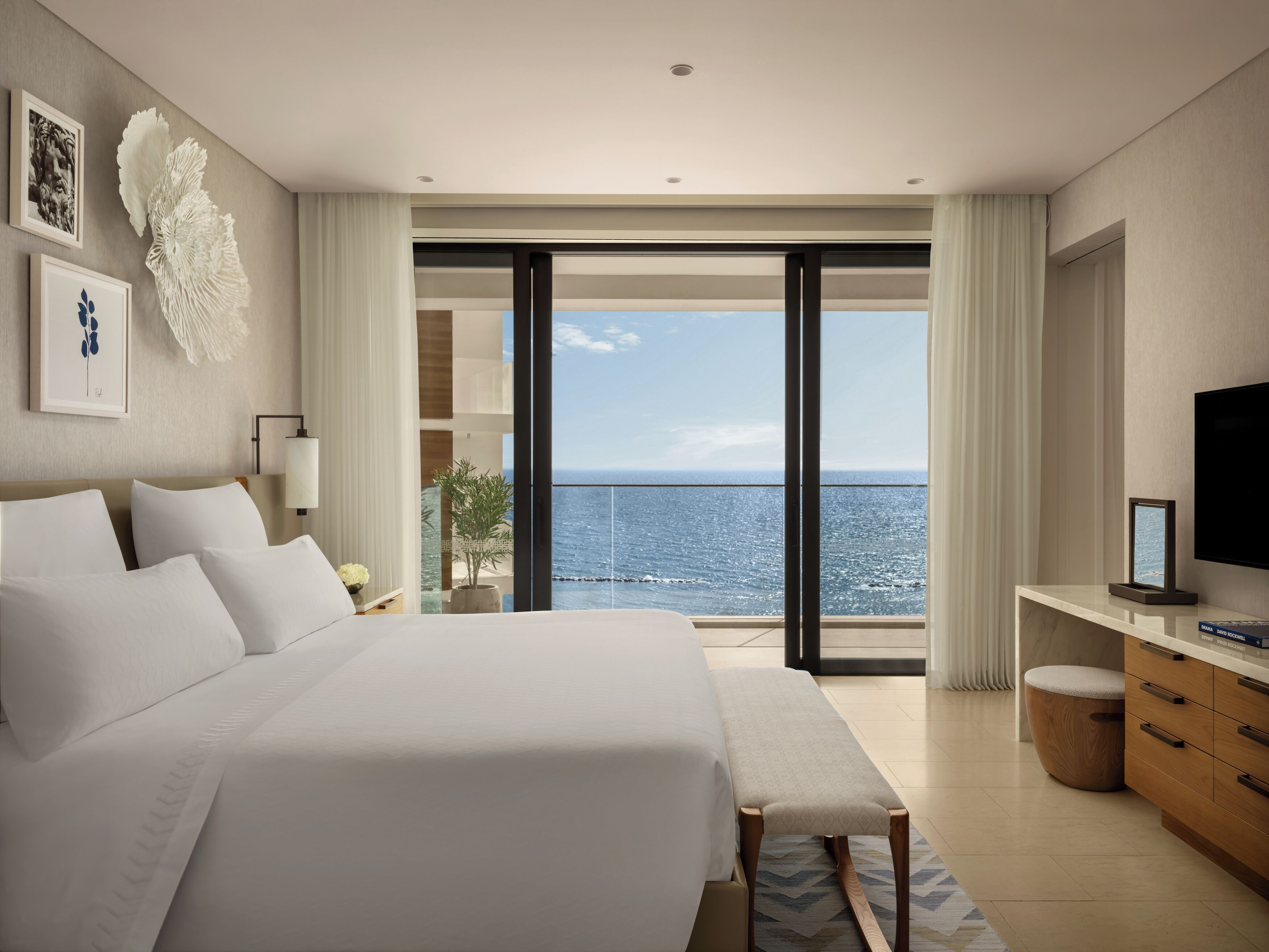 Une chambre à coucher moderne avec un grand lit, un banc, une télévision et une vue sur la mer.
