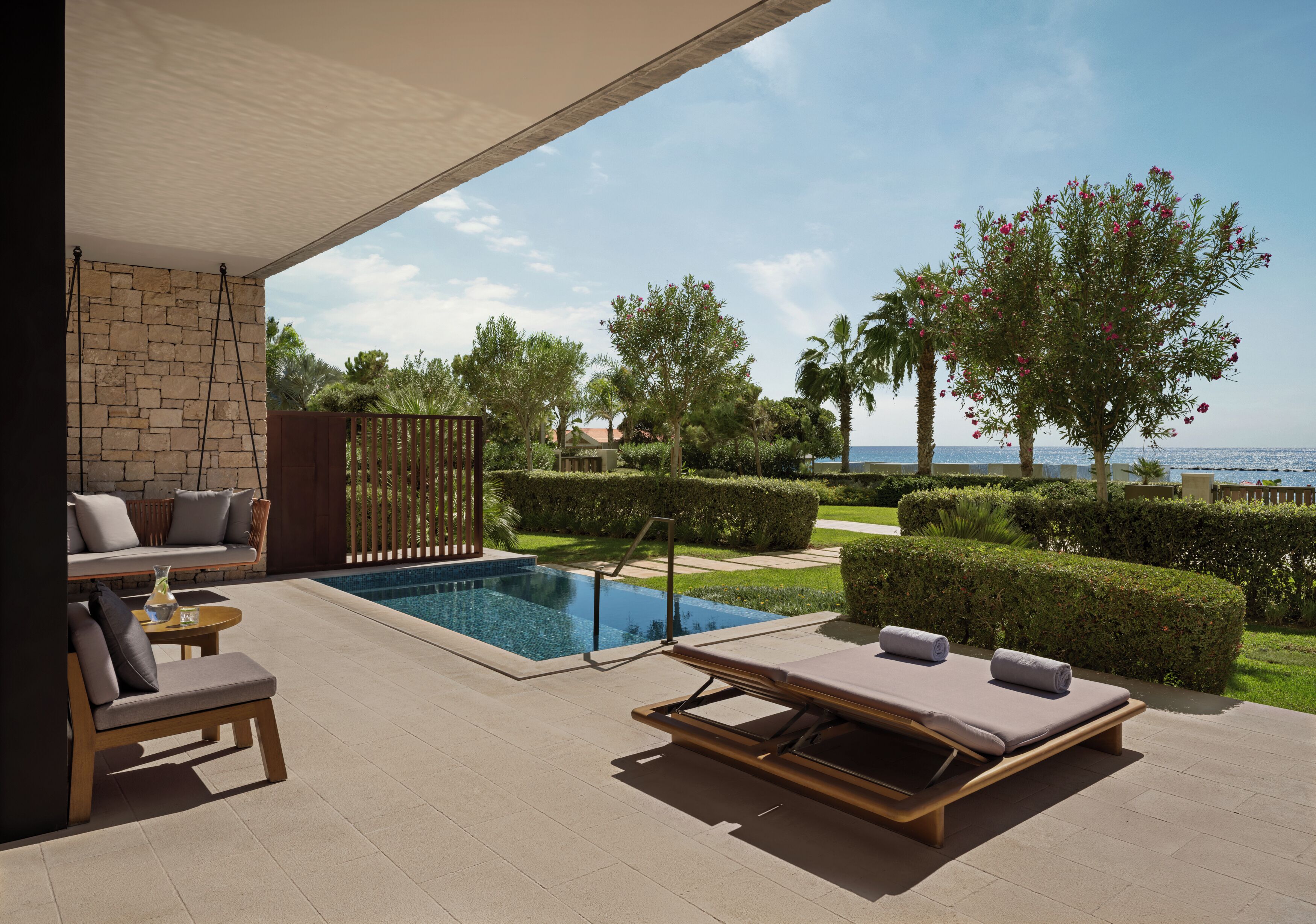 A poolside area with lounge chairs, a small table, and a view of the sea.