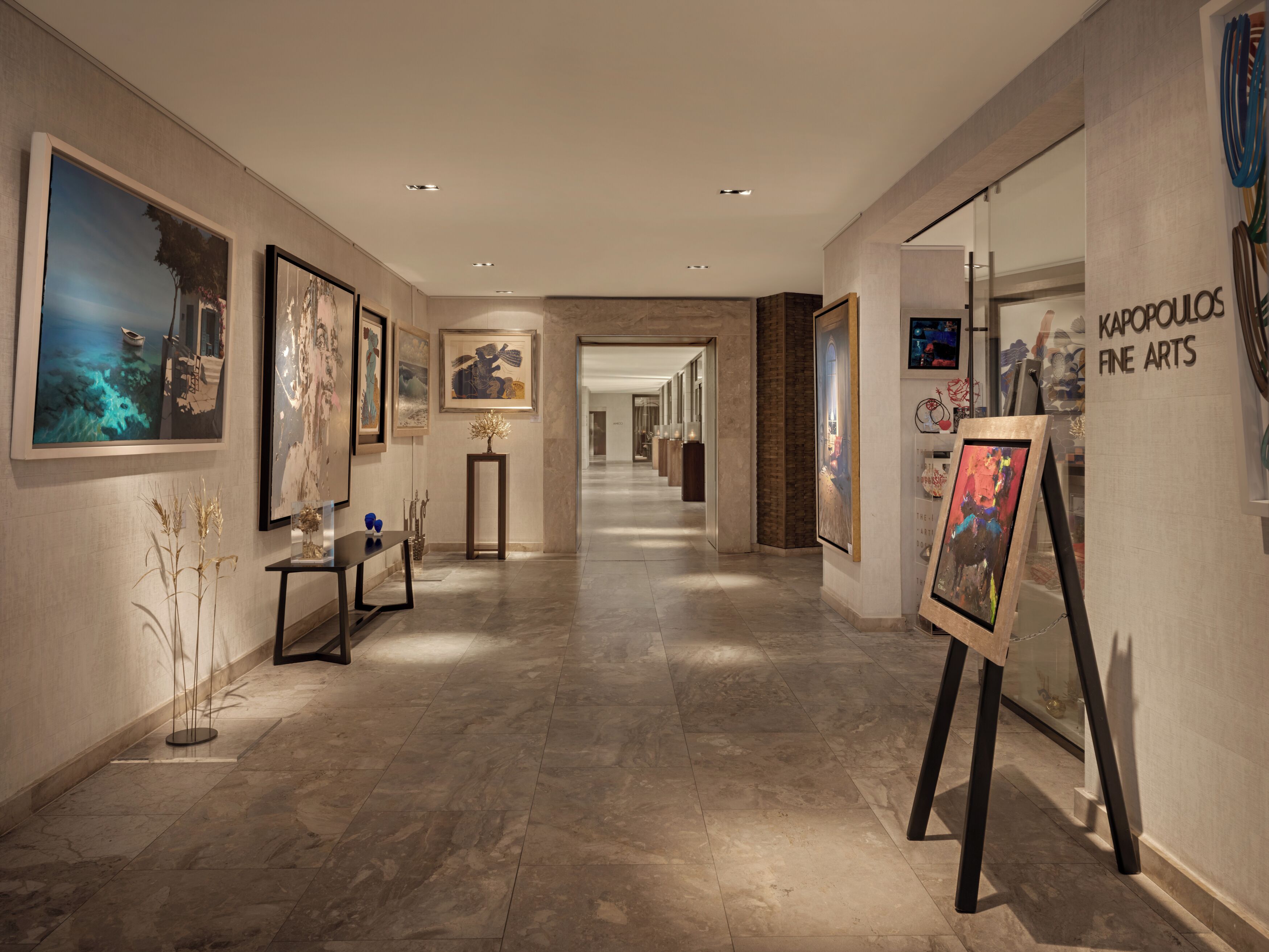 A hallway with art displays, a marble floor, and a sign for 'KAPOPOLLOS FINE ARTS'.