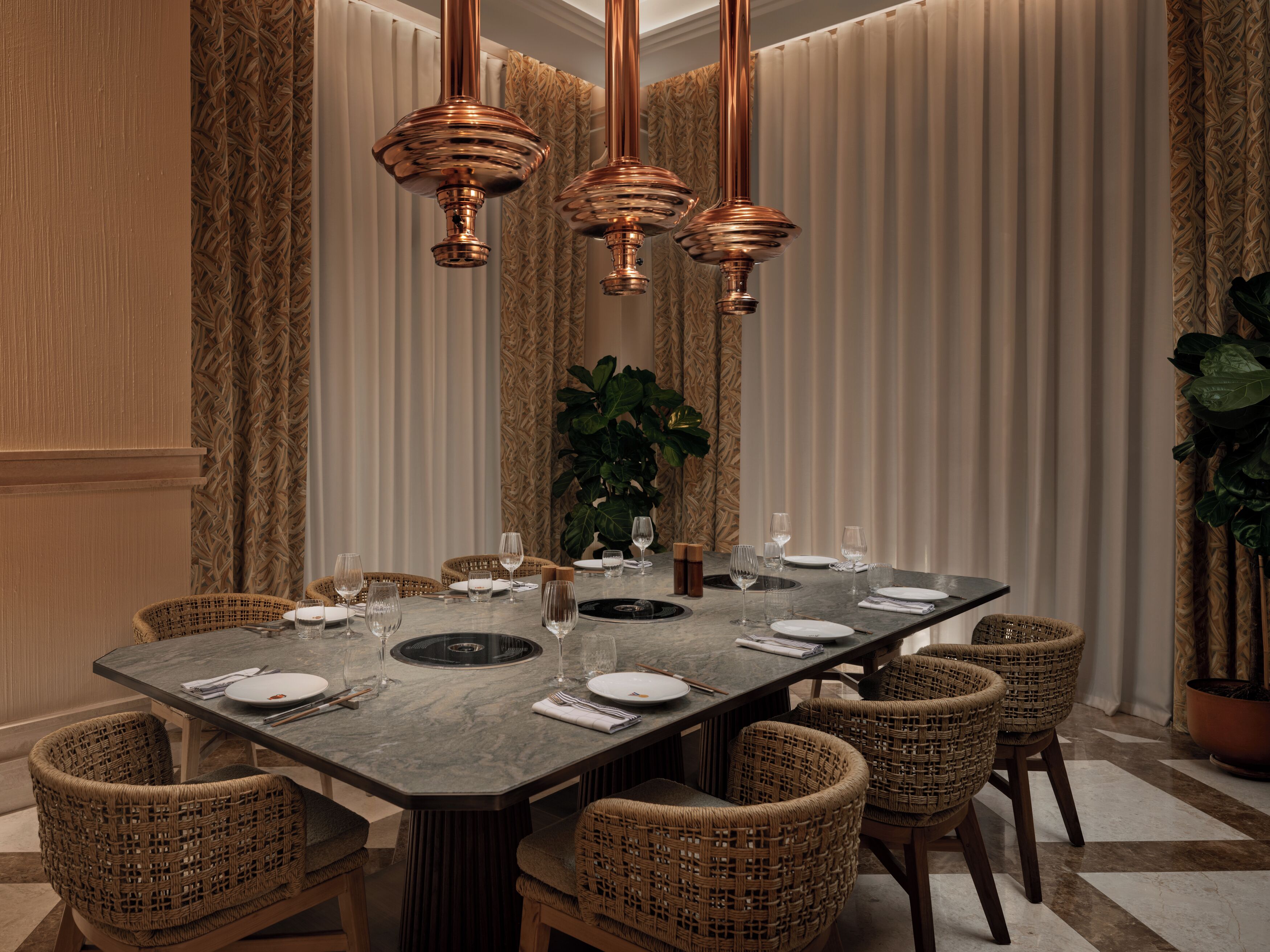 A dining area with a rectangular table, wicker chairs, and copper pendant lights.