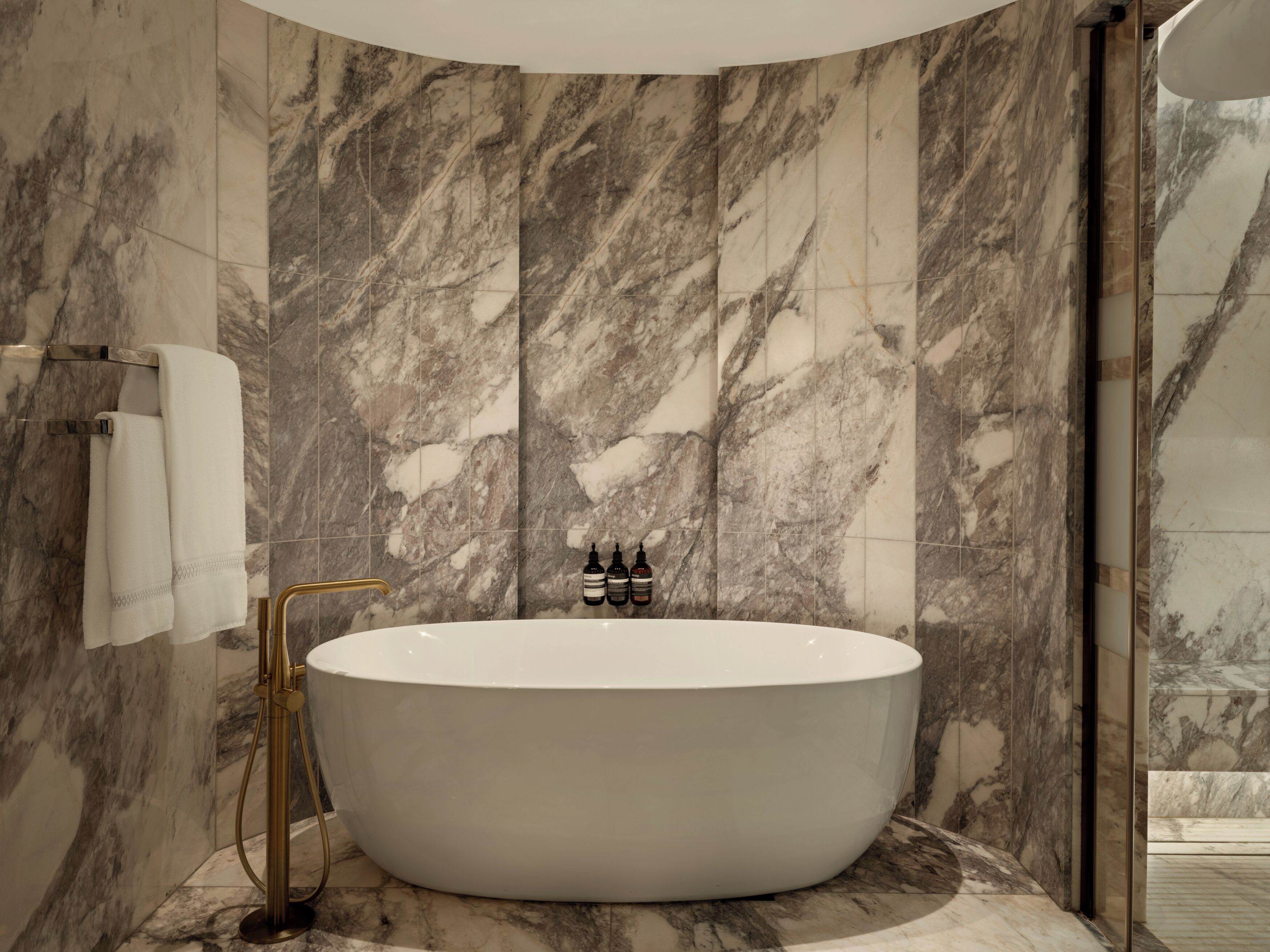 Une salle de bain moderne avec une baignoire sur pieds, des murs en marbre et un robinet doré.