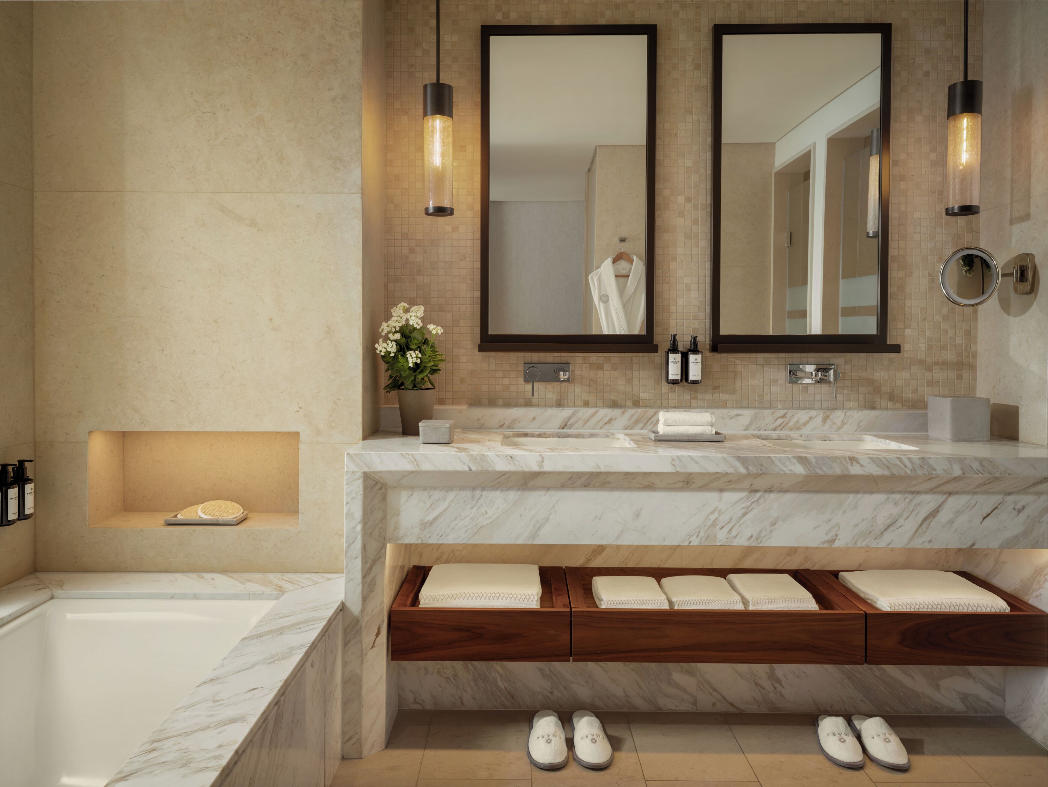 A modern bathroom with a marble vanity, dual mirrors, a built-in bench with towels, and a bathtub.