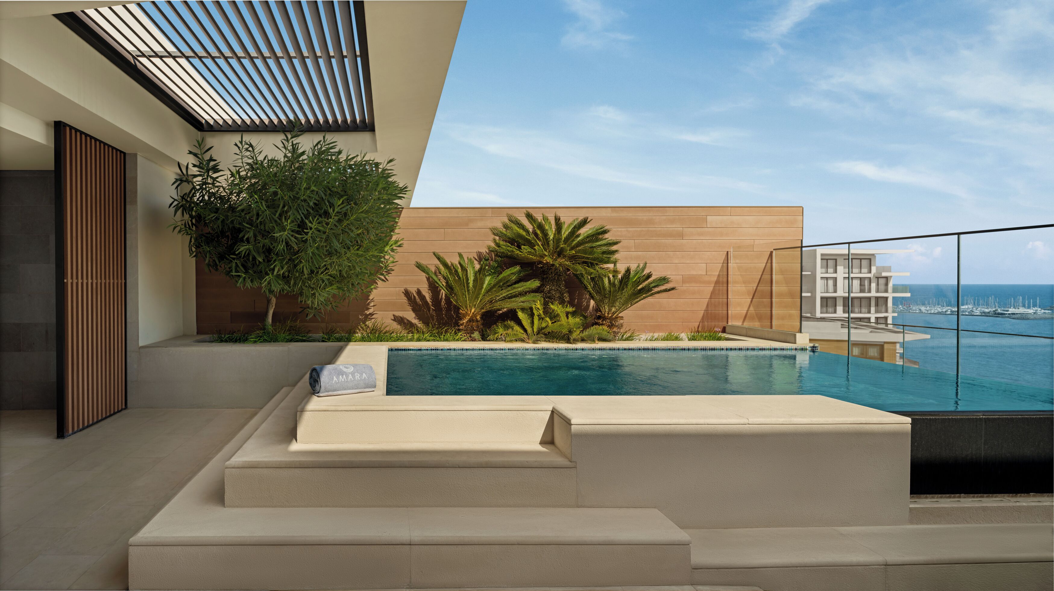 Zona de piscina moderna al aire libre, con vista al océano y un edificio al fondo.