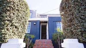 Ein modernes Haus mit blauer Fassade, einem weißen Vorgatter und einer Treppe aus roten Ziegelsteinen, die zum Eingang führt.