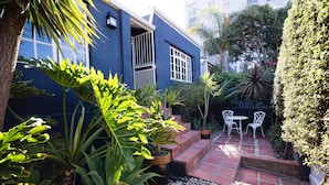 Ein blaues Haus mit Terrasse, Blumentöpfen und Gartenmöbeln.