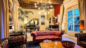 A cozy living room with a grand piano, leather sofas, and a large window with a view. - Villa Troletti, hôtel particulier de luxe en provence  (L'Isle-sur-la-Sorgue)
