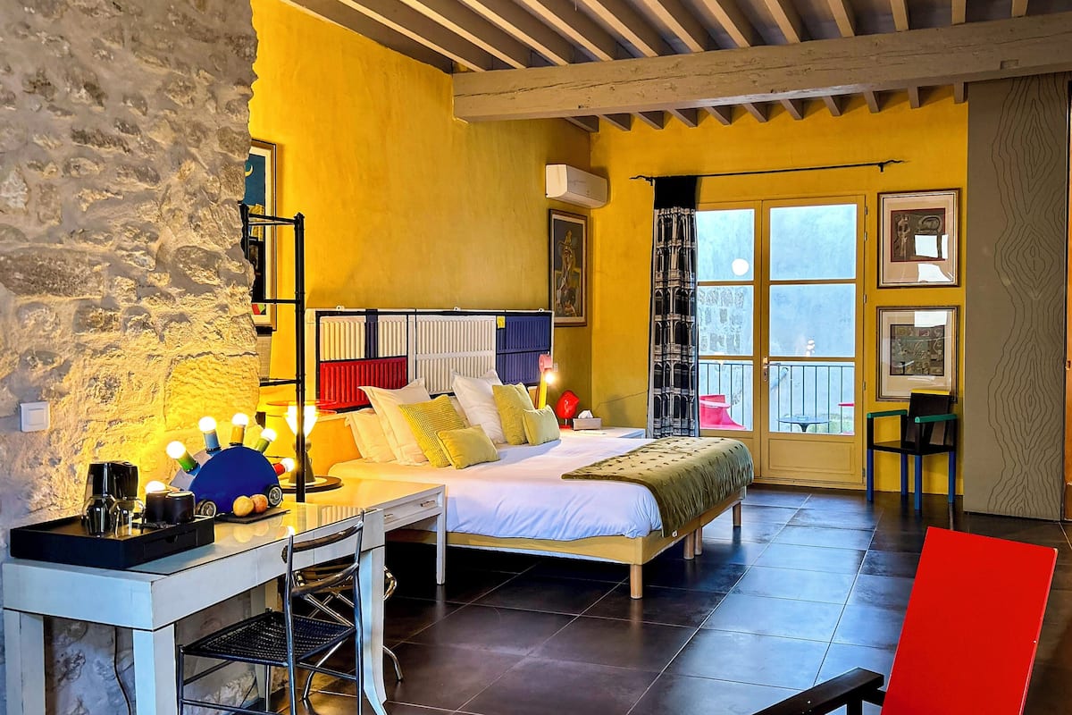 Un dormitorio con cama, mesita de noche, lámpara y ventana con vistas.
