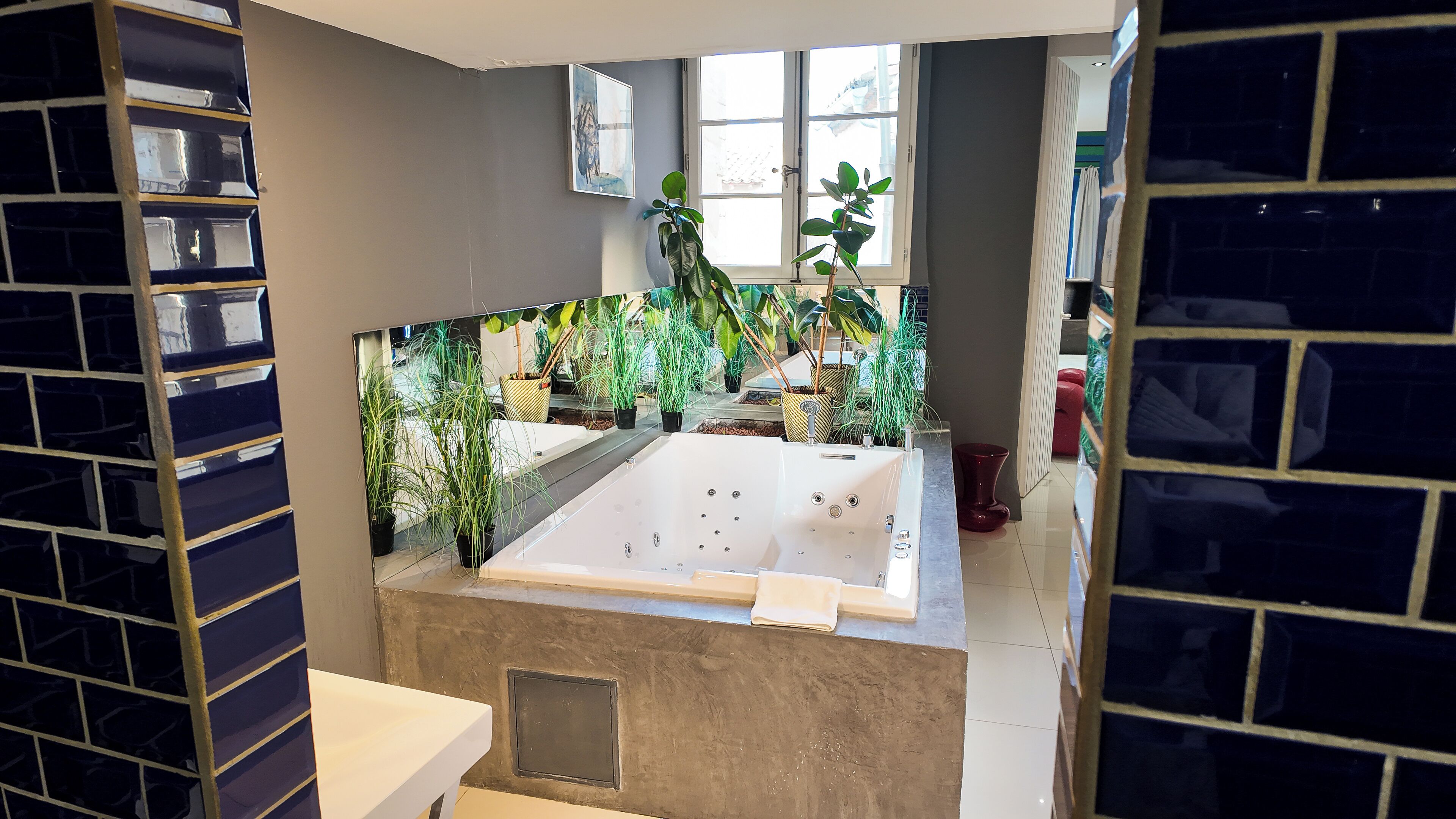 Une salle de bain avec une grande baignoire, des plantes en pot et un mur carrelé.