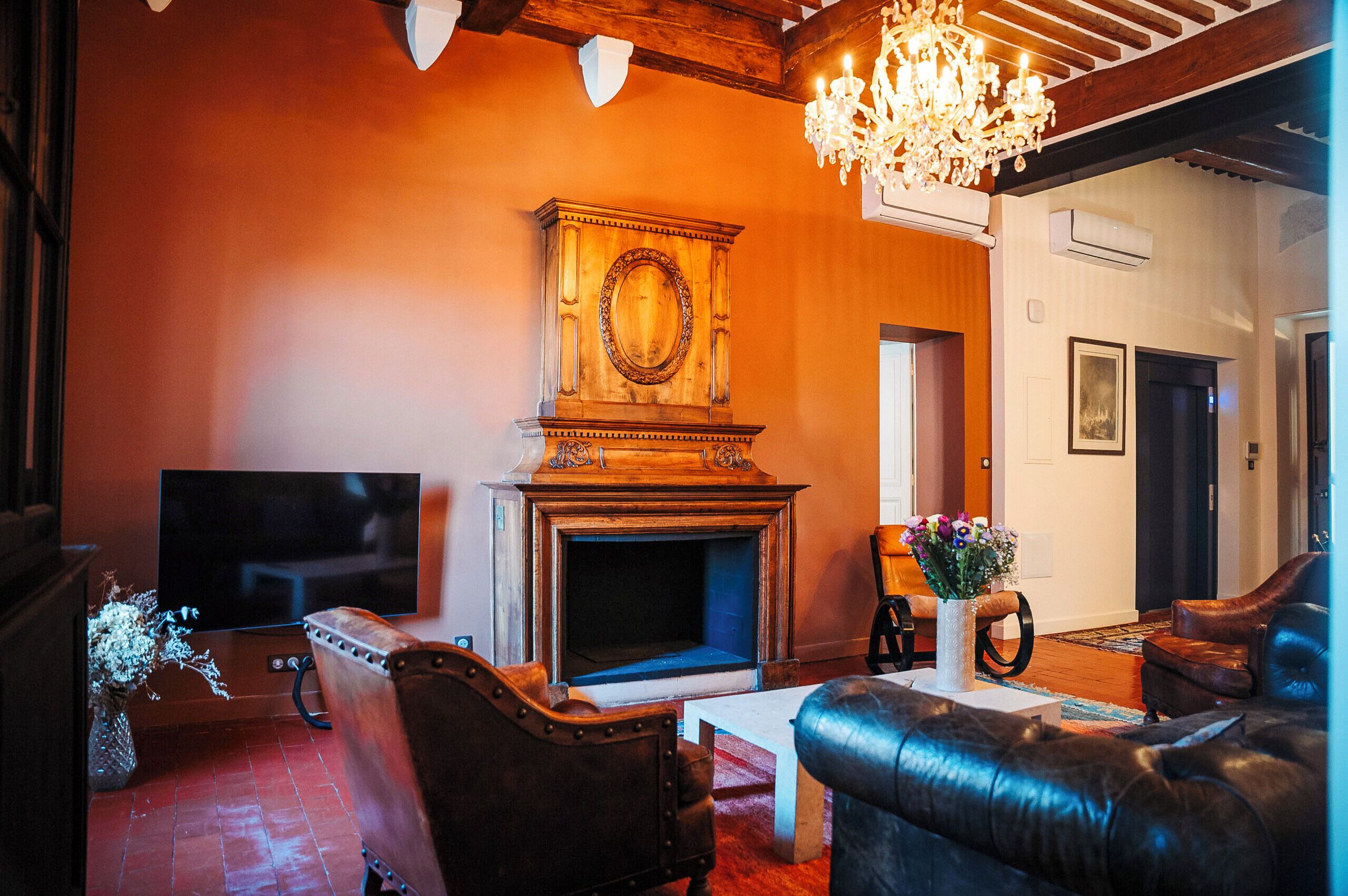 A living room with a fireplace, leather sofas, a television, and a chandelier.