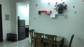 A dining area with a table and four chairs, a refrigerator, a small shelf with a clock, and a potted plant on the wall. - Nancy Sweet Apartment (Ho Chi Minh City)