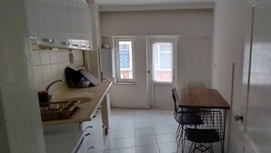 A compact kitchen with white cabinets, a wooden countertop, and a dining area with a table and chairs. - Ada Kale Pansiyon (Çanakkale)