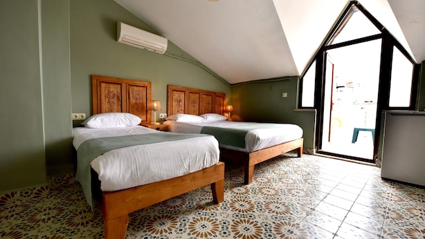 A room with two wooden beds, a tiled floor, an air conditioning unit, and a view through a window. - Ada Kale Pansiyon (Çanakkale)