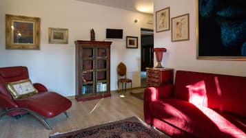 A living room with a red sofa, a red armchair, a wooden cabinet, and a red vase.