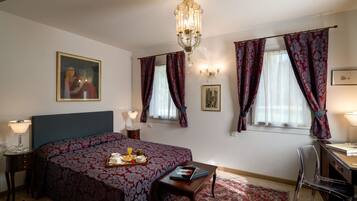 Una camera d'albergo con un grande letto, una scrivania, una sedia, un lampadario e opere d'arte alle pareti.