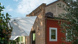Un edificio moderno con fachada de ladrillo y detalles en rojo, que cuenta con un patio amueblado con mesas y sombrillas.