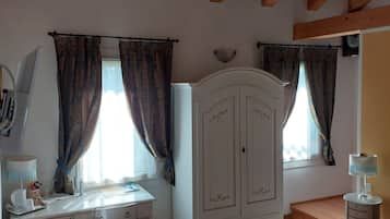 A bedroom with a wooden ceiling, a desk with a lamp, a wardrobe, and a bed with a patterned bedspread.