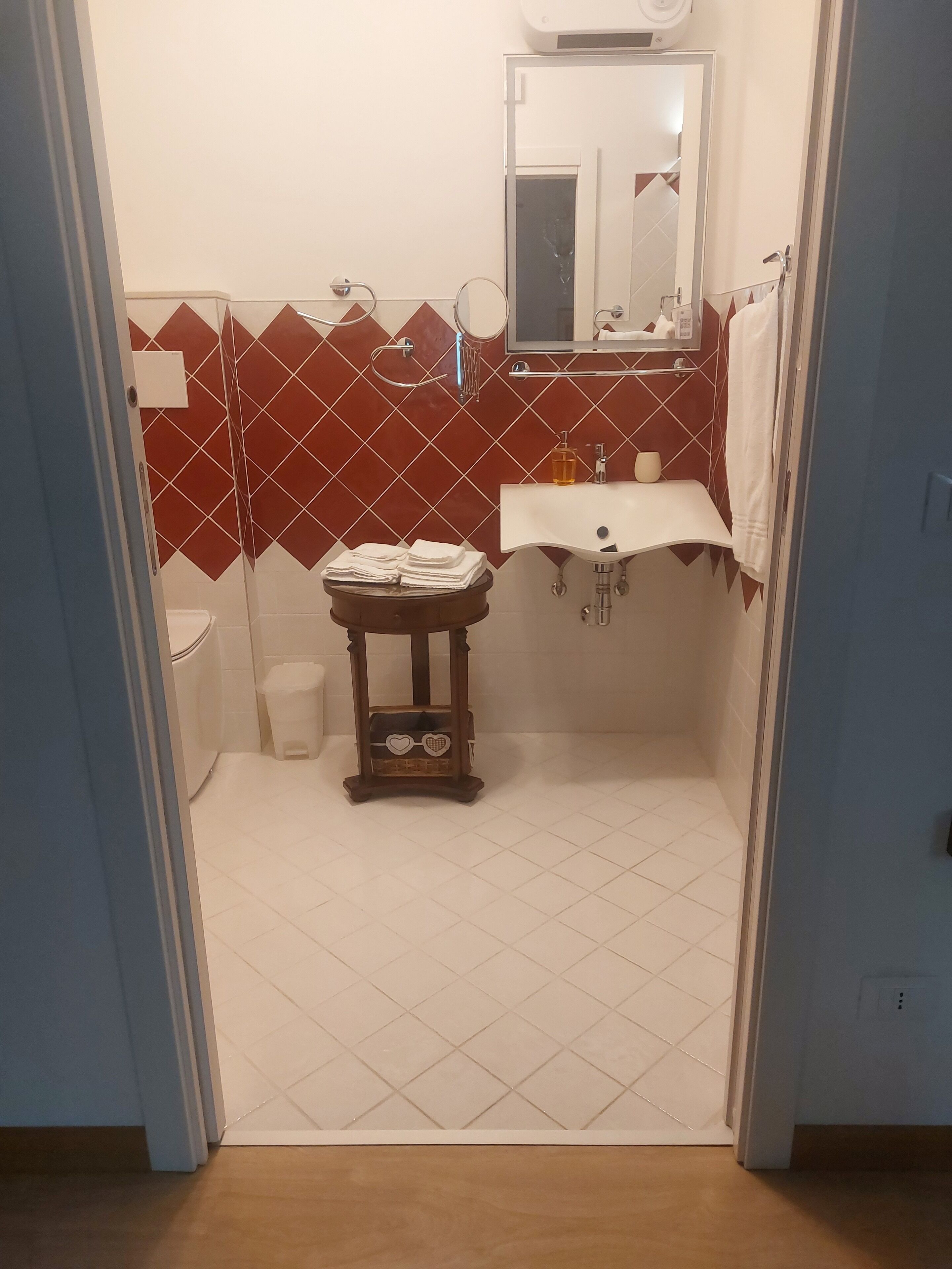 A bathroom with a white sink, red diamond-patterned tiles, a wooden vanity, and a mirror above the sink.