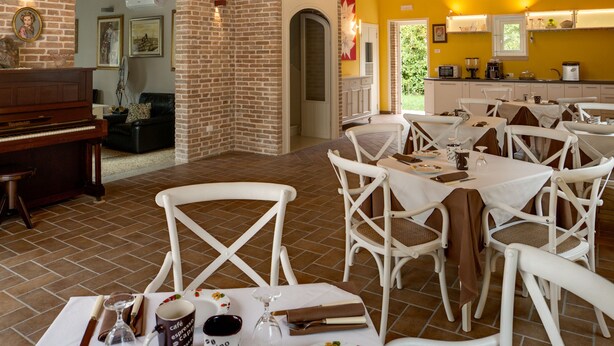 Comedor con sillas y mesas blancas, un piano y una pared de ladrillo.