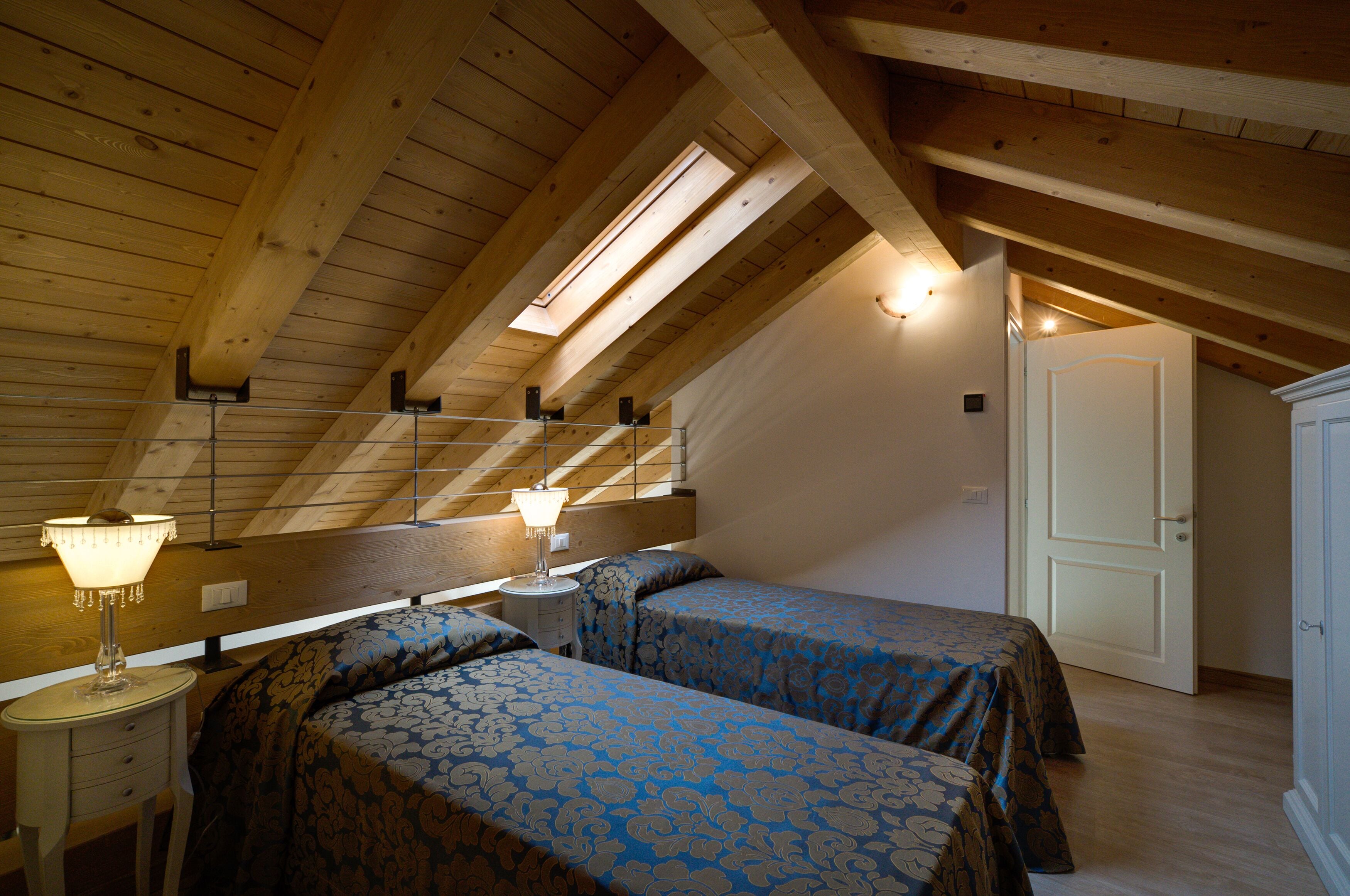 A bedroom with two beds, wooden beams, a skylight, and a nightstand with a lamp.
