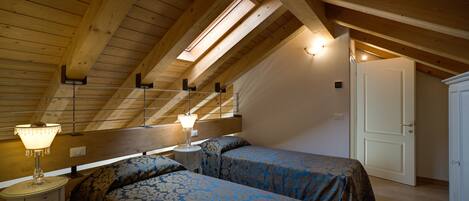 Un dormitorio con dos camas, vigas de madera, un tragaluz y una mesita de noche con lámpara.