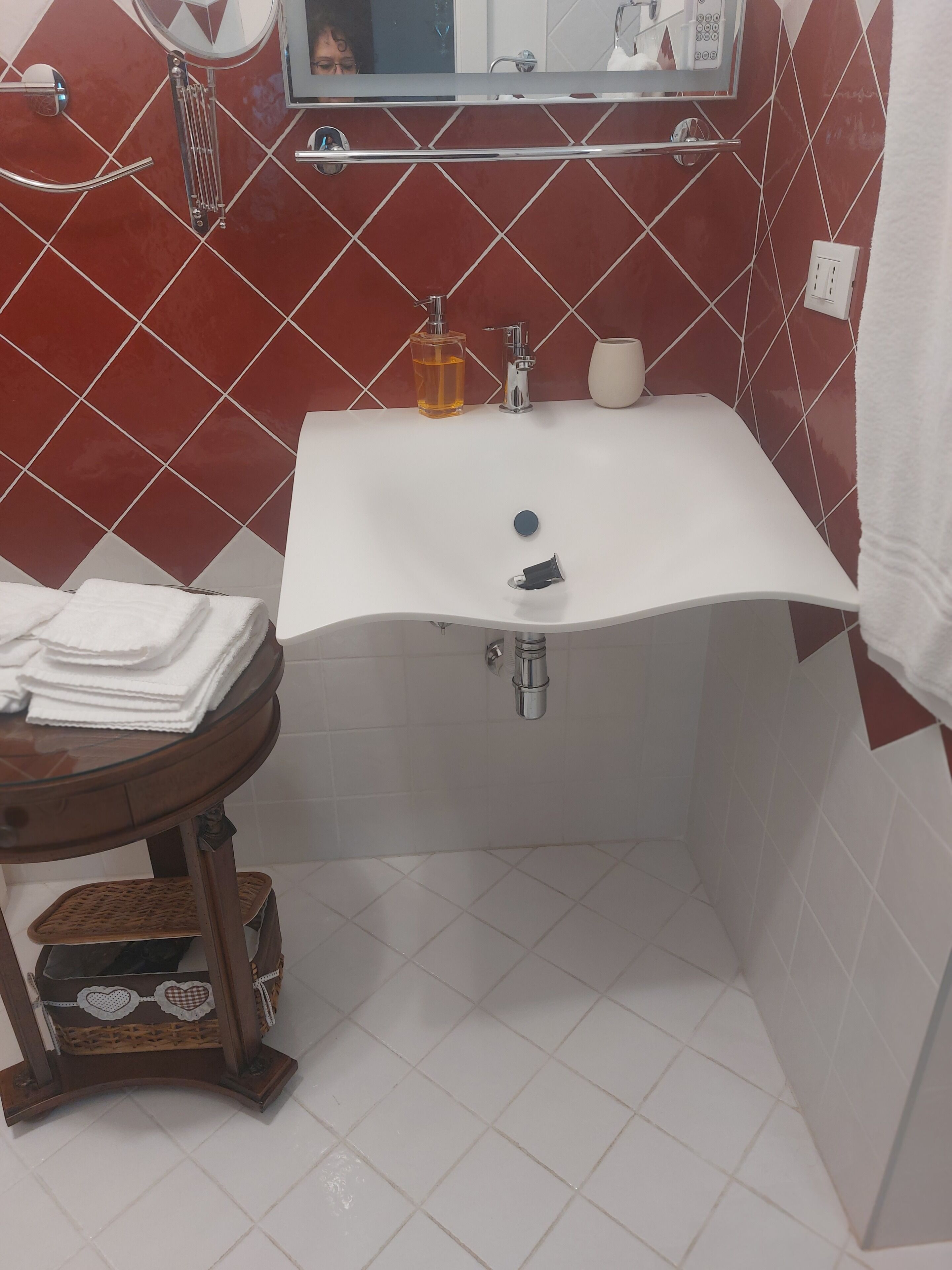 Un baño con un lavabo blanco, paredes con azulejos rojos, un espejo y un perchero para toallas.