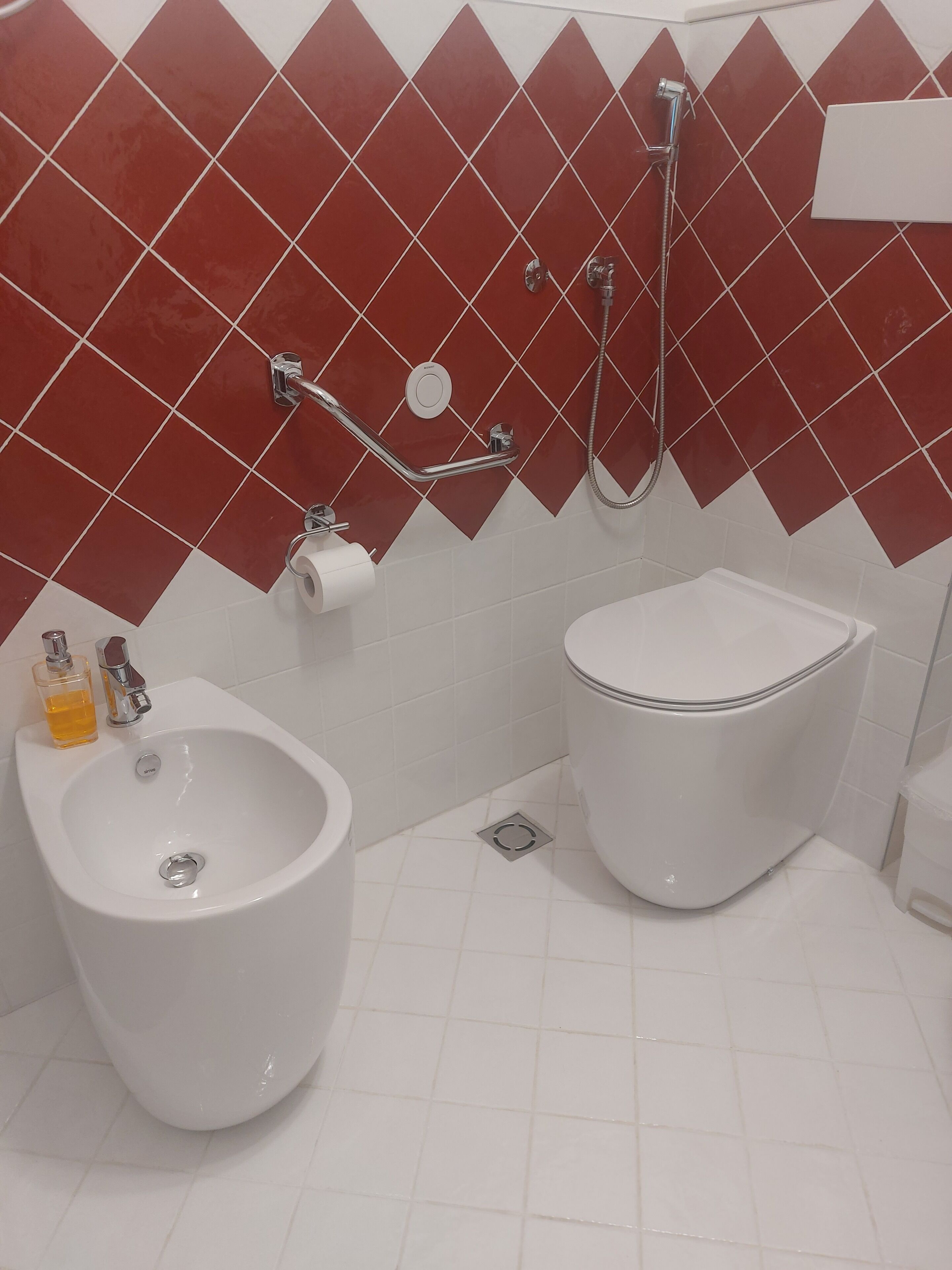 Un baño con bidé, inodoro y lavabo con una botella de jabón.