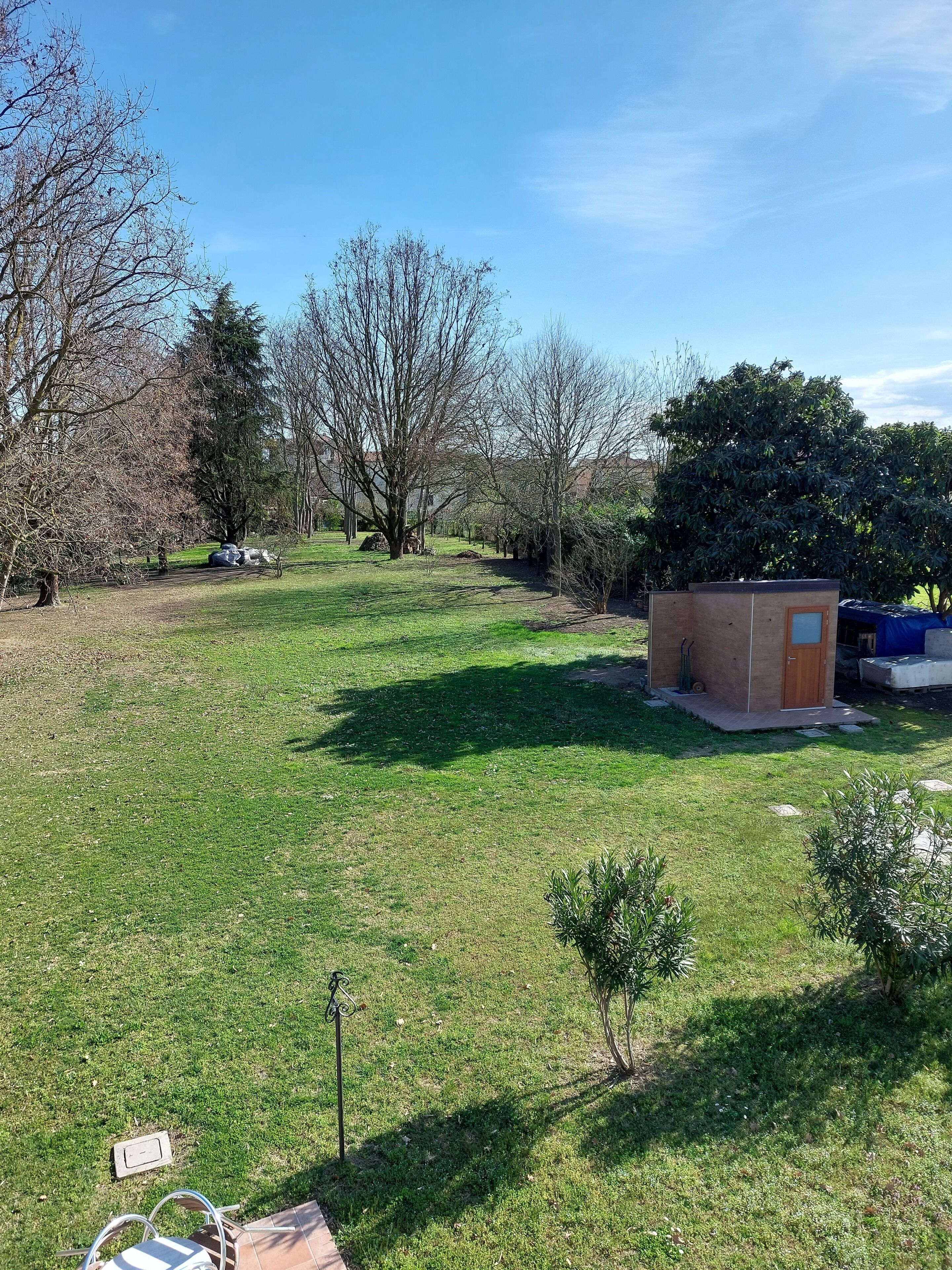 Un espacio al aire libre con césped, una pequeña construcción de ladrillo, posiblemente un cobertizo o almacén, y una silla de metal.