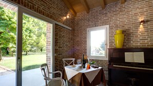 Comedor con piano, una mesa dispuesta con platos y vista a un jardín a través de un ventanal.