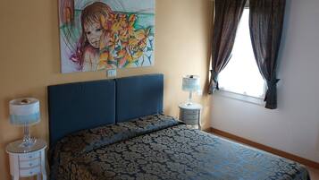 Une chambre à coucher avec un lit, une table de chevet, une lampe, une fenêtre avec des rideaux et un tableau au mur.