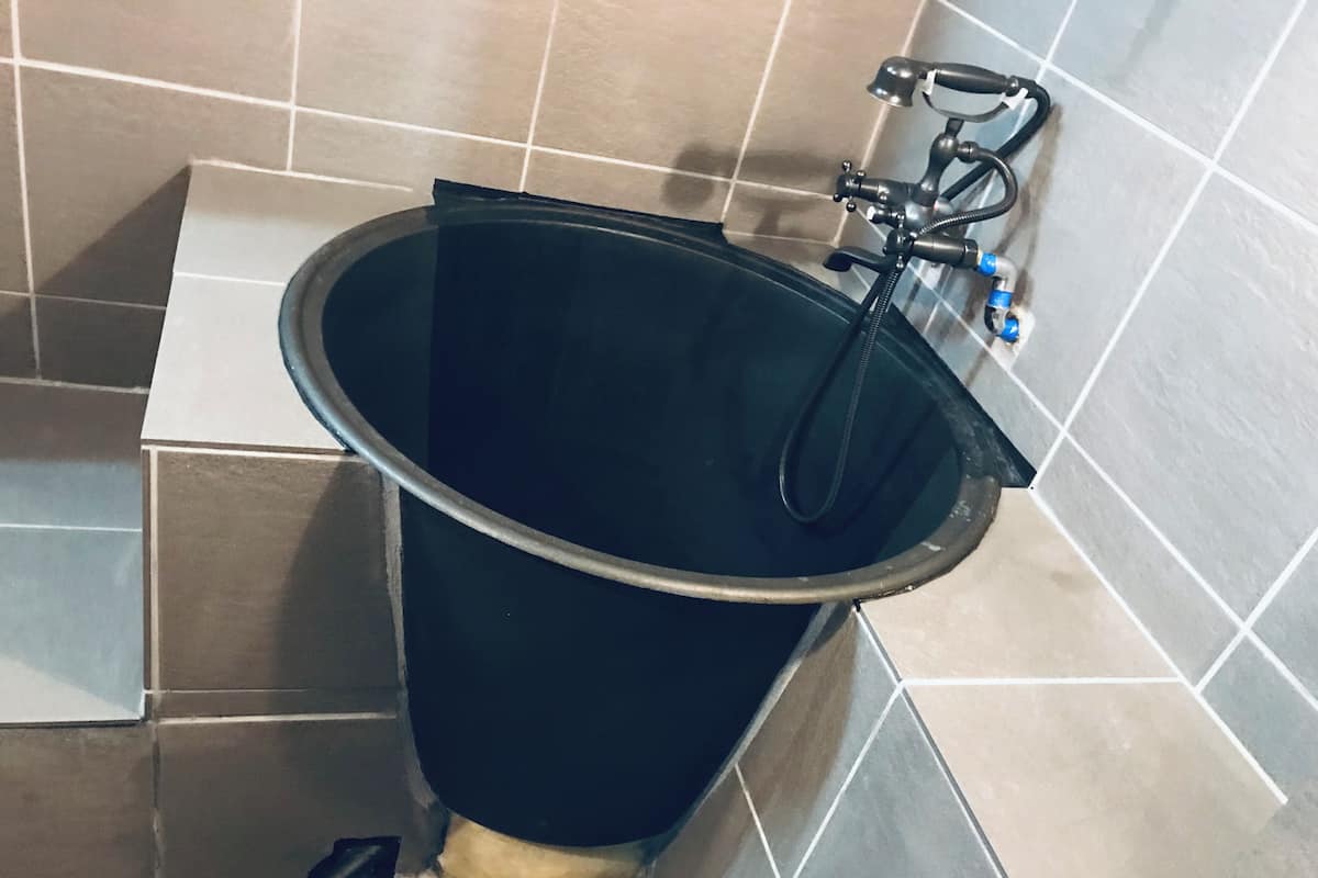 A bathroom with a black bathtub, a handheld showerhead, and a handheld faucet.