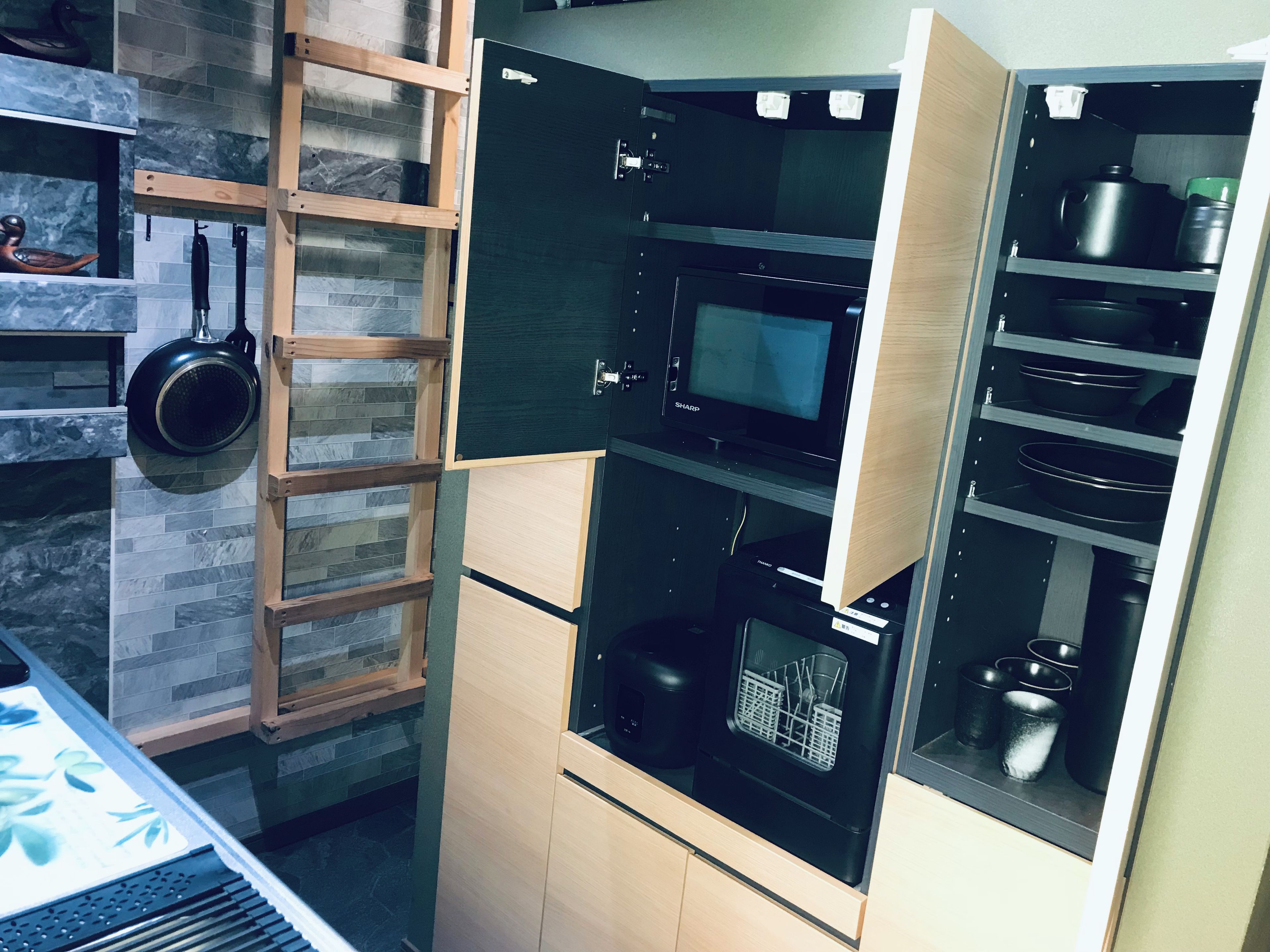 A kitchen with a microwave, oven, and a wooden shelf with a pan.