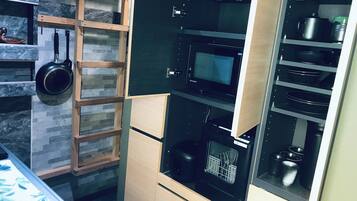 A kitchen with a microwave, oven, and a wooden shelf with a pan.