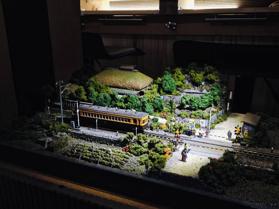 A model train layout with a train station, tracks, and surrounding greenery.