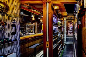 A bar with a wooden interior, a visible smoking area sign, and a staircase leading to an upper level. - Koke Musu inn (Otsu)